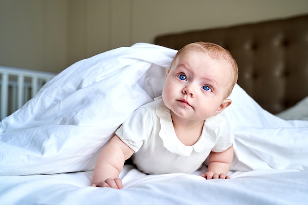 Un petit enfant aux yeux bleus se trouve sur un lit blanc