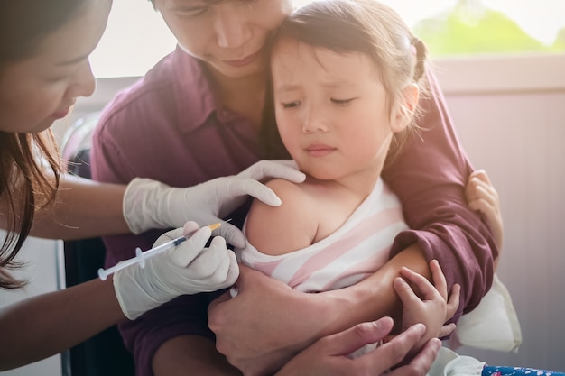 Petit enfant, avoir, injection, gros plan, docteur, injection, vaccination, à, bras, de, asiatique, petite fille, à, les, père, étreindre l'enfant, pour ne pas se tortiller pendant l'injection de vaccination