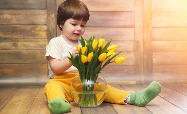 Un petit enfant avec un bouquet de tulipes jaunes. Un garçon avec un cadeau de fleurs dans un vase. Un cadeau pour les filles en vacances avec des tulipes jaunes sur le sol.