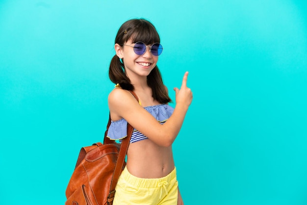 Petit enfant caucasien allant à la plage isolé sur fond bleu pointant vers l'arrière