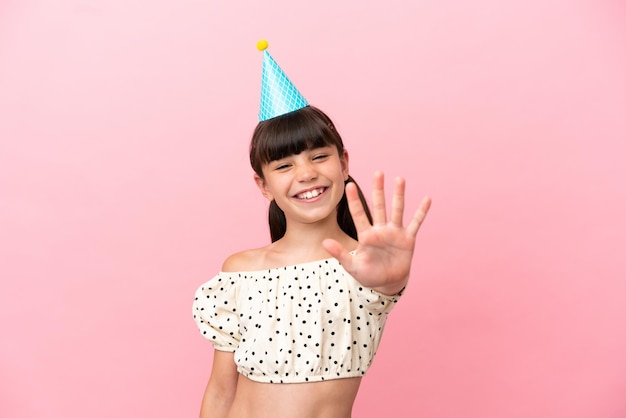 Petit enfant caucasien avec chapeau d'anniversaire isolé sur fond rose comptant cinq avec les doigts