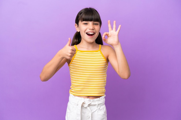 Petit enfant caucasien isolé sur fond violet montrant un signe ok et un geste du pouce vers le haut