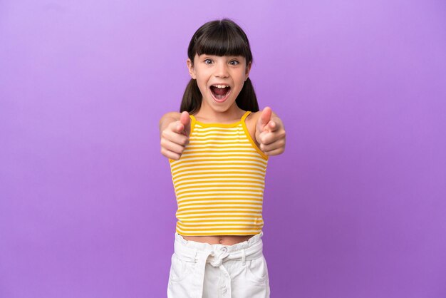 Petit enfant caucasien isolé sur fond violet surpris et pointant vers l'avant