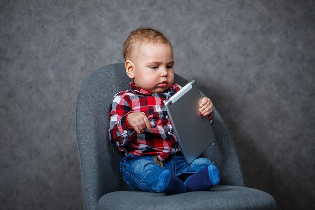 Un petit enfant en chemise joue avec une tablette