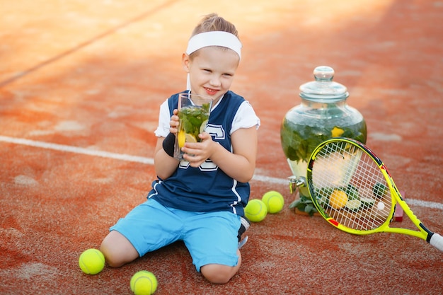 Petit Enfant En Costume De Tennis Assis Sur Un Court De Tennis En