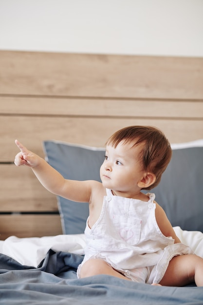 Petit enfant curieux assis sur le lit et pointant du doigt