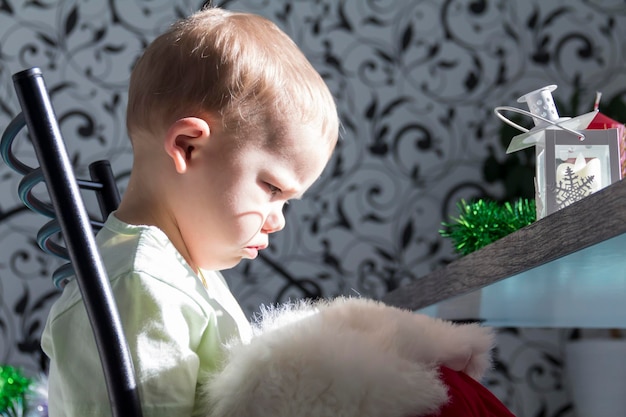 Un petit enfant dans un chapeau de Père Noël et des mitaines rouges avec des cadeaux de Noël est assis à la table du Nouvel An