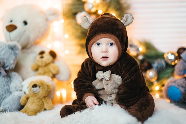 Un petit enfant dans un costume d'ours en peluche marron est assis sur le sol