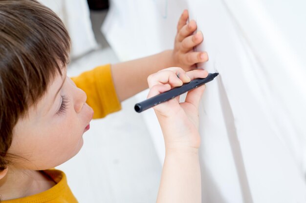 Un petit enfant dessine sur un tableau blanc avec un feutre Activités à domicile en auto-isolement