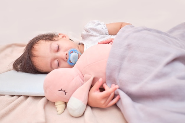 Petit enfant de faire une sieste au lit tout en serrant dans ses bras un jouet moelleux en peluche se réveiller avec une sucette dans sa bouche