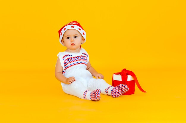 Le petit enfant fête Noël. Bébé en costume du Nouvel An avec un cadeau sur fond jaune.