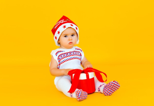 Le petit enfant fête Noël. Bébé en costume du Nouvel An avec un cadeau sur fond jaune.