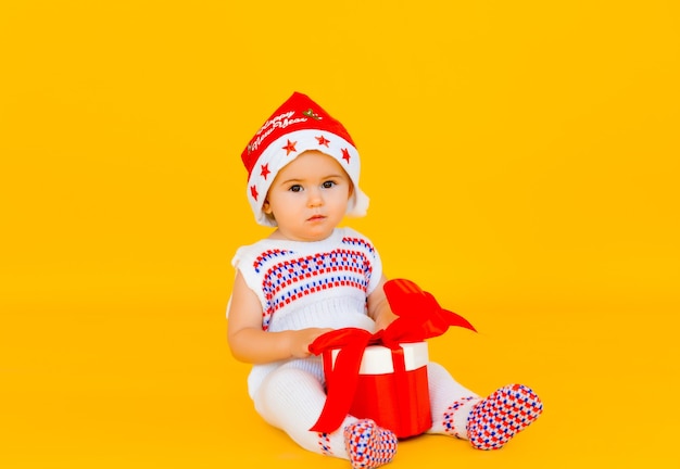 Le petit enfant fête Noël. Bébé en costume du Nouvel An avec un cadeau sur fond jaune.