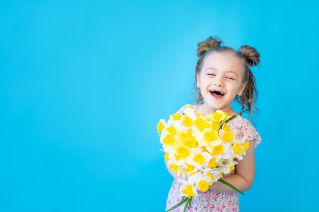 Un petit enfant fille sur un fond de studio isolé bleu avec des fleurs de printemps jaune jonquilles Espace pour copier du texte