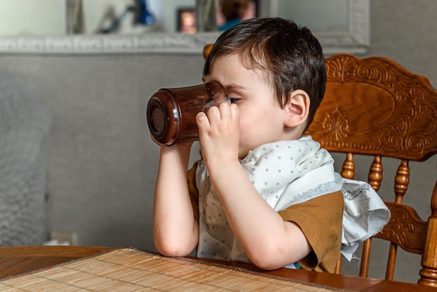 Un petit enfant garçon boit tout seul dans une tasse