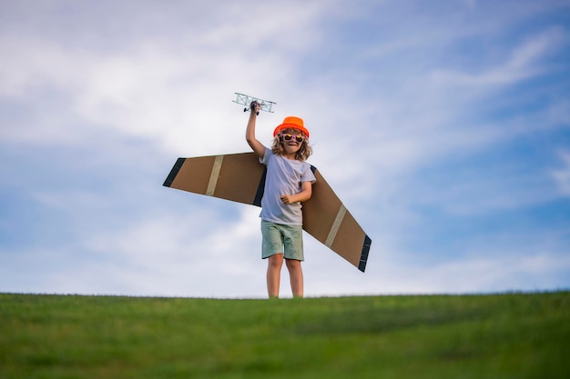 Petit enfant garçon joue et rêve de voler au-dessus des nuages Enfant aviateur pilote avec un avion jouet joue sur la nature estivale Enfant jouant avec des ailes d'avion Concept de rêves et de voyages