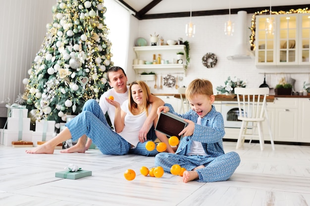 Un petit enfant garçon en pyjama bleu assis sur un sol ouvrant une boîte-cadeau avec des mandarines