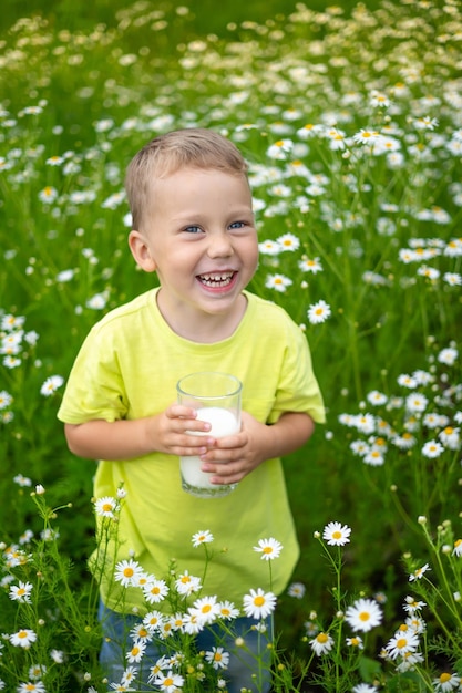 Un petit enfant un garçon vêtu de vêtements en coton naturel se promène sur le terrain tient un verre de lait dans ses mains profite de la vie profite de la nature