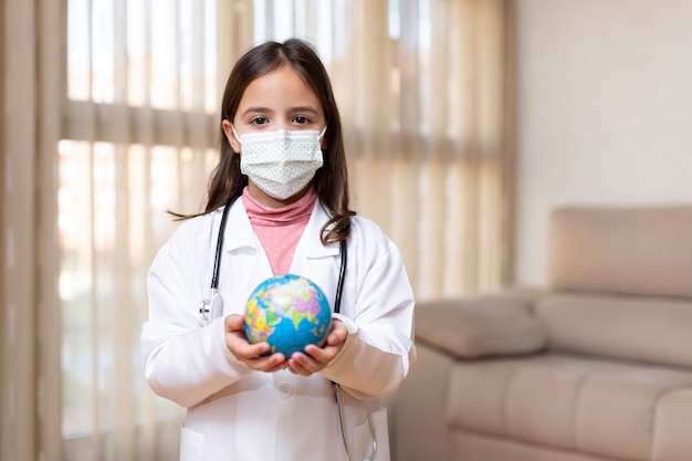 Petit enfant habillé en médecin avec un masque médical tenant une boule du monde dans ses mains