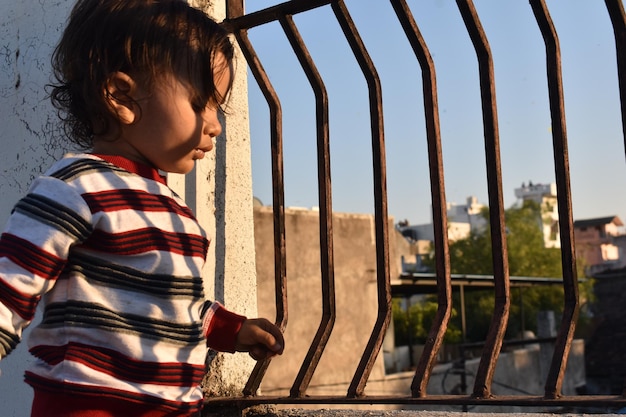 Petit enfant indien se tenant aux barres de balcon et regardant dehors