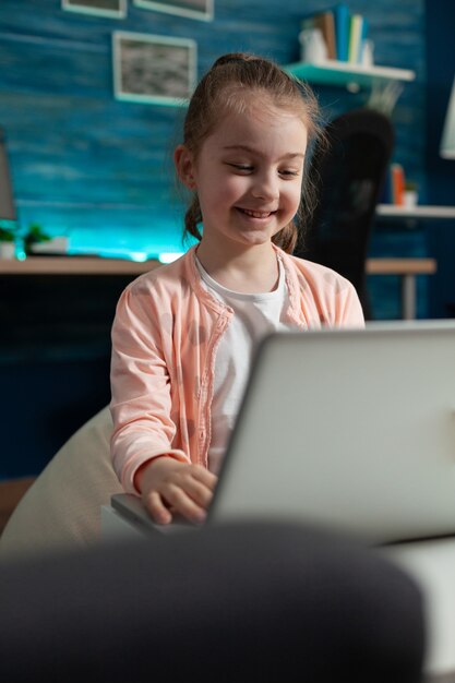 Petit enfant intelligent tapant sur un ordinateur portable moderne au bureau à domicile