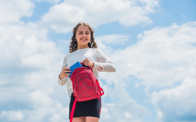 Petit enfant en journée ensoleillée temps de vacances d'été petit enfant souriant au printemps temps fille bouclée heureuse tenir sac à dos sur fond de ciel retour à l'école bonheur de l'enfance Concentré sur l'étude