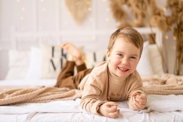 Un petit enfant sur un lit dans des tons naturels marron beige rit et se réjouit un petit enfant joyeux et drôle joue à la maison