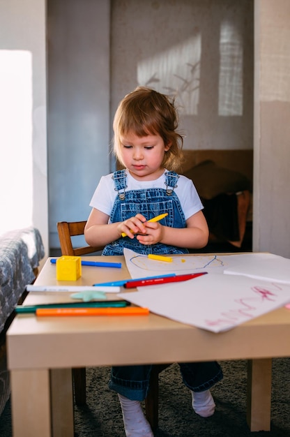 Petit enfant à la maison à la table des enfants dessine avec des feutres