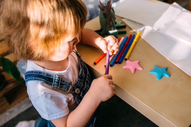 Petit enfant à la maison à la table des enfants dessine avec des feutres