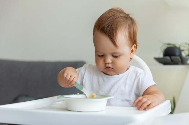 Un petit enfant mange assis à la table des enfants.