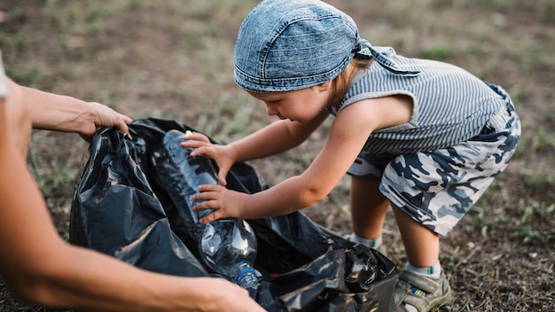 Petit enfant met une bouteille en plastique dans un sac poubelle