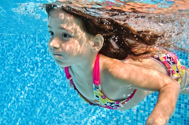 Petit enfant nage sous l'eau dans la piscine, heureux bébé fille active plonge et s'amuse sous l'eau