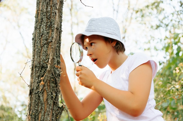 Un petit enfant naturaliste botaniste avec une loupe est surpris et choqué explore l'écorce des arbres
