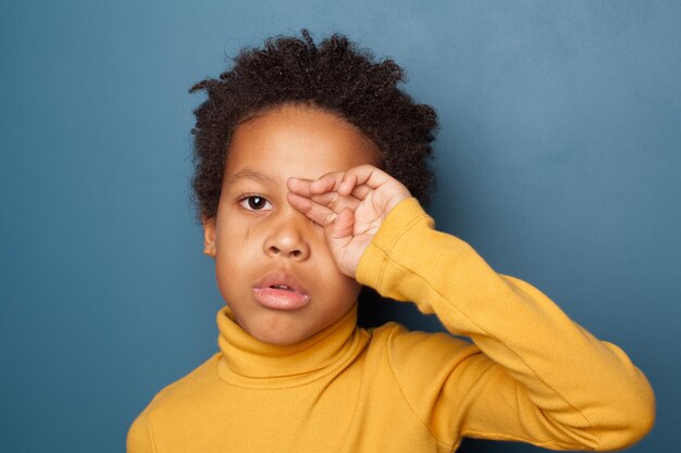 Un petit enfant noir fatigué et malheureux pleure sur un fond bleu.