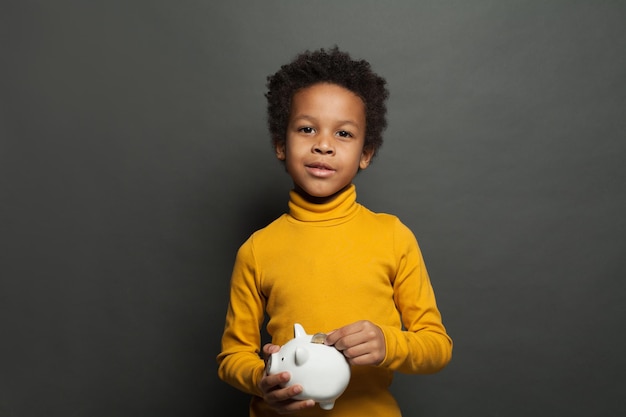 Photo petit enfant noir tenant une boîte à argent et une pièce sur fond de tableau noir