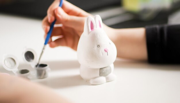 Petit enfant peignant la figure de lapin de Pâques en céramique. Enfant faisant du bricolage. Atelier ou master class.