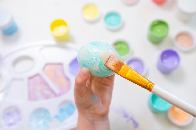 Un petit enfant peint des oeufs de Pâques en fille de couleur azur préparant des décorations pour Pâques