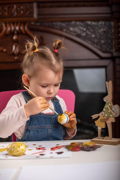 Un petit enfant peint des oeufs avec des peintures colorées pour Pâques