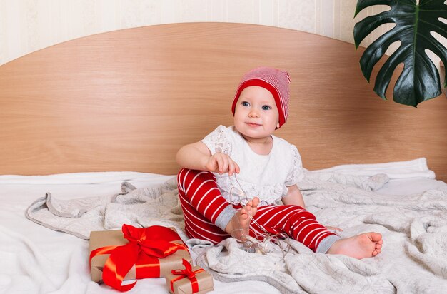 Petit enfant portant un chapeau de Santa helper est assis sur le lit avec un cadeau