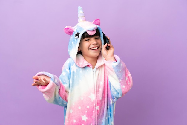 Petit enfant portant un pyjama licorne isolé sur fond violet gardant une conversation avec le téléphone portable avec quelqu'un