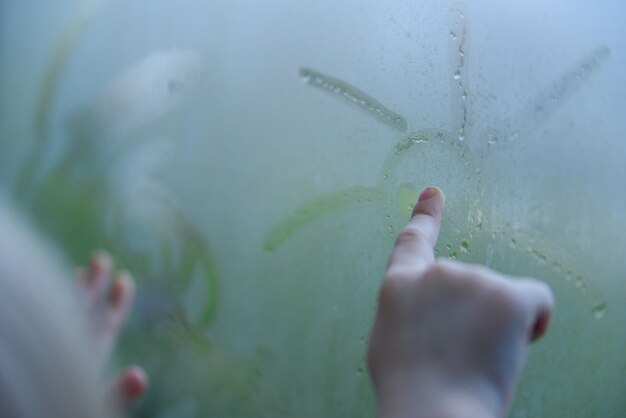 Le petit enfant près de la fenêtre. Un enfant un jour de pluie attire le soleil sur la fenêtre embuée.