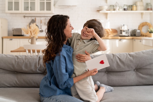 Petit enfant présente la carte de voeux de maman avec le coeur le jour d'anniversaire de la fête des mères embrassant les vacances de la Saint-Valentin