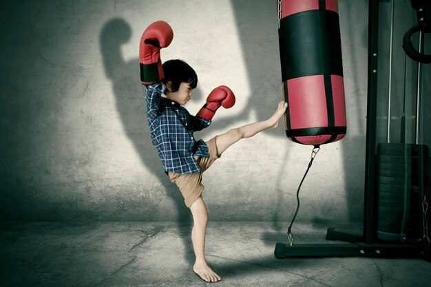 Photo un petit enfant qui donne un coup de pied à un sac de boxe dans le studio.