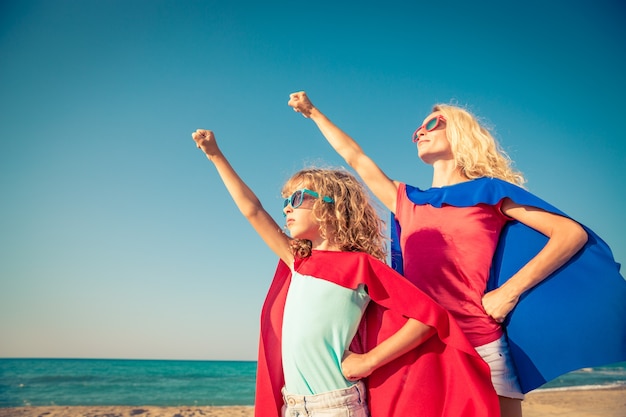 Petit enfant et sa maman déguisés en super-héros levant les bras sur la plage