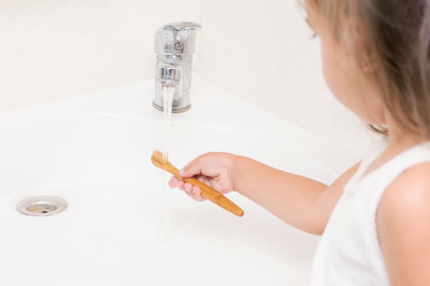 Un petit enfant se brosse les dents avec une brosse à dents en bambou.