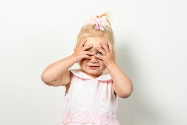 Petit enfant se couvre le visage avec ses mains sur un fond clair.