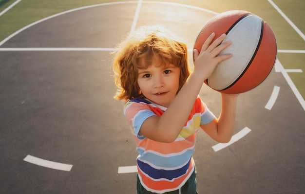 Petit enfant de sport caucasien jouant au basket-ball tenant le ballon avec un portrait de visage heureux de drôle sportif