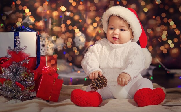 Petit enfant surpris dans un chapeau de père Noël. Garçon sur un novoodney guirlandes de surface avec des boîtes avec des cadeaux et une bosse dans sa main.