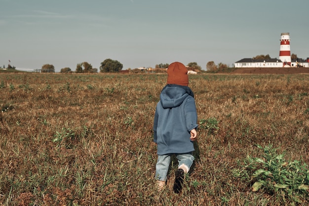 Un petit enfant traverse le champ dans le contexte du phare, un enfant a deux ans. Promenades d'automne dans la nature.