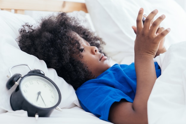 Photo petit enfant utilisant un smartphone avec réveil comptant trop de temps le matin